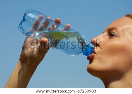 woman drinking water from a plastic bottle outside in summer