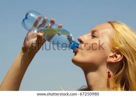 woman drinking water from a plastic bottle outside in summer