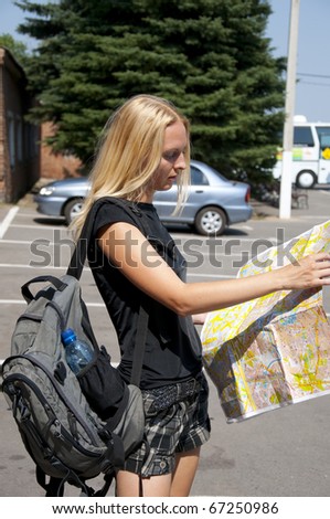 The blonde girl-traveler with a map of the city and a backpack in the street.