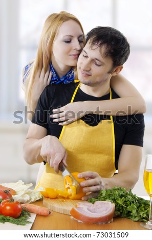 young attractive loving couple embracing face to face in light kitchen. Man cut vegetables