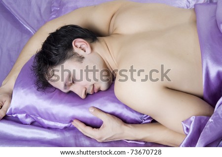 Young beautiful sleeping man with nude muscular back at bedroom on silk sheet