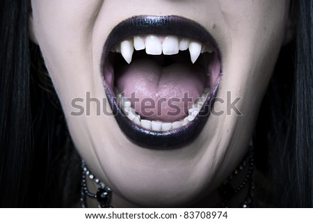Opened mouth with long white fangs closeup of screaming vampire woman. Make up for halloween