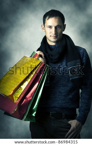 Portrait of a young man wearing scarf and dark blue shirt after shopping with bags