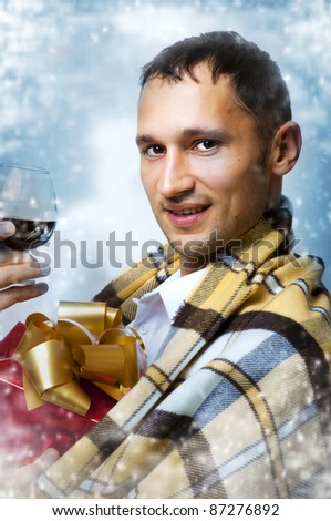 Christmas. Young adult handsome man with glass of old brandy and red gift box with gold ribbon