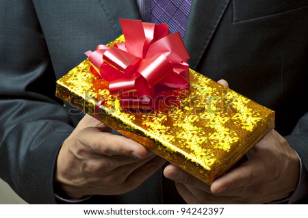 Male hands holding gift. Present in golden box with red ribbon