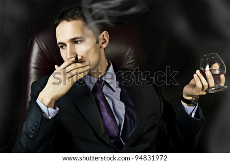 portrait of young handsome business man with Old Brandy Glass in hand and smoking cigar on black background. men\'s club