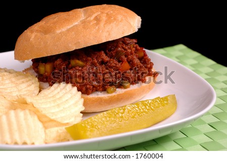 Sloppy Joe sandwich with chips and pickle on a white plate and bright green mat