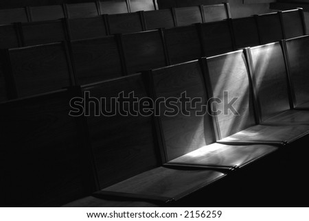 Black and white image of Rows of church pews with stream of light illuminating a seat
