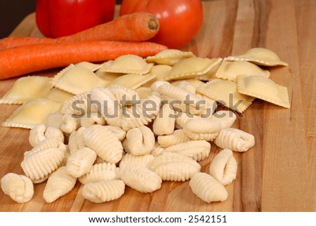 Gnocchi and ravioli on a cutting board with vegetables in background