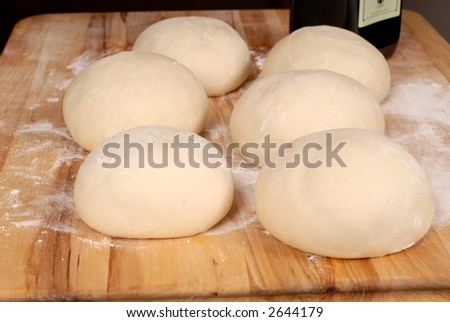 Six balls of freshly made pizza dough on floured cutting board