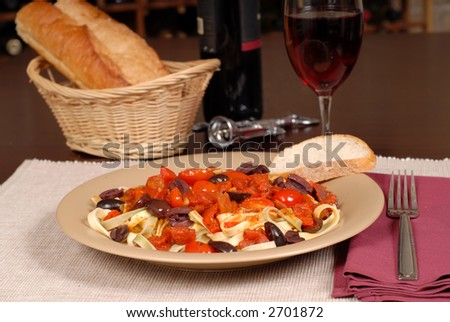 Plate of pasta puttanesca with wine and bread