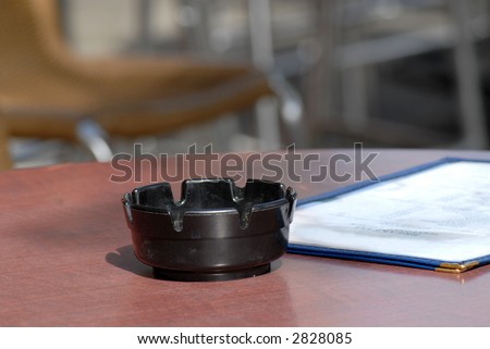 An ashtray and menu on a table in a sidewalk cafe dining area