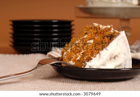A piece of carrot cake with plates in background