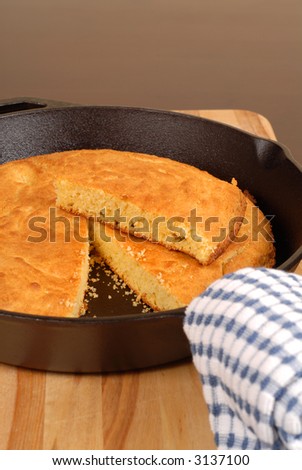 Cornbread in a cast iron skillet with piece cut out vertical view