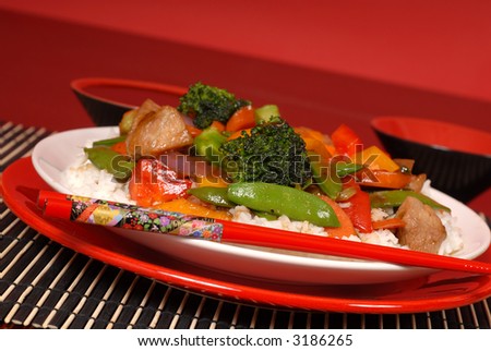A plate of stir fry pork with chop sticks in a red theme