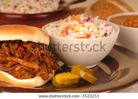 A pulled pork sandwich with cole slaw and beans