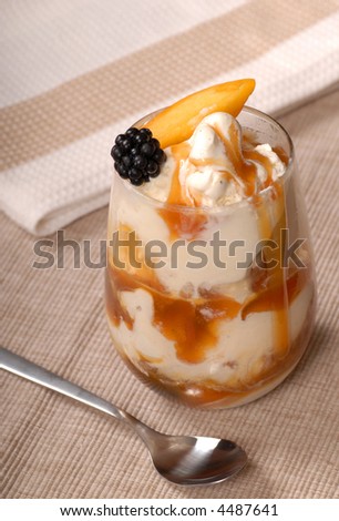 A glass of vanilla ice cream with blackberries, peaches, and a caramel sauce