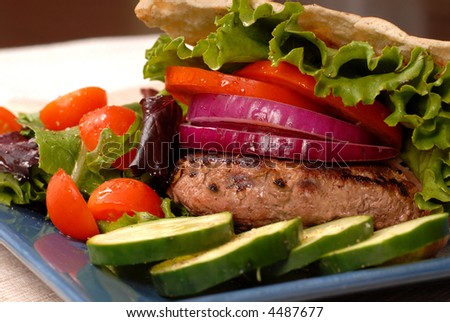 Grilled hamburger in a pita bread with a salad and cucumbers