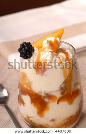 A glass of vanilla ice cream with peaches, blackberries and caramel sauce