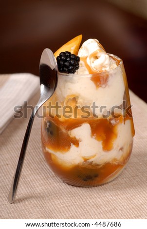 Vanilla ice cream with blackberries, peaches, and caramel sauce on a brown background