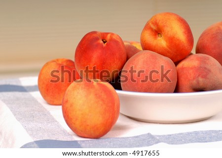 A bowl of fresh ripe peaches on a white and blue cloth