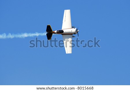 A white airplane performing stunts at an air show leaving a trail of smoke