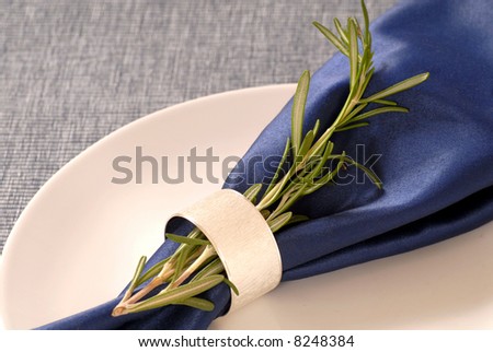 A napkin with rosemary herbs held in place by a silver napkin ring