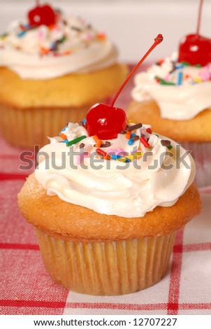 Delicious golden cupcakes with vanilla buttercream, sprinkles and maraschino cherry