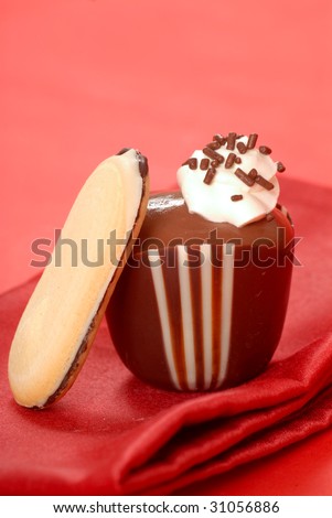 Chocolate pudding in a dark and white chocolate cup with whipped cream and a cookie