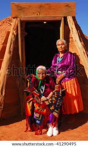 Elderly 99 year old Navajo Native American woman and her daughter standing in front of a traditional Hogan