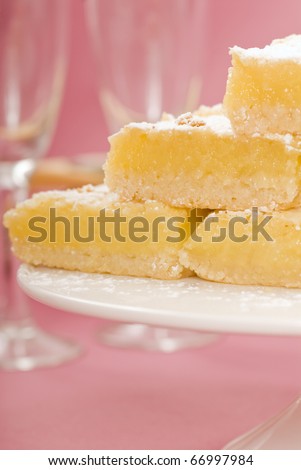 Delicious freshly baked lemon squares on a white cake stand with Champagne glasses in the background