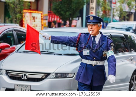 KOBE, JAPAN - NOVEMBER 17: Security Guard in Kobe, Japan on November 17, 2013. Unidentified security guard raises a red flag at a traffic lights for people to cross the street at Motomachi street