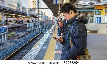 TOKYO, JAPAN - NOVEMBER 22: People on a platform in Tokyo, Japan on November 22, 2013. Unidentified Japanese male uses his device while waits for a train on a plateform