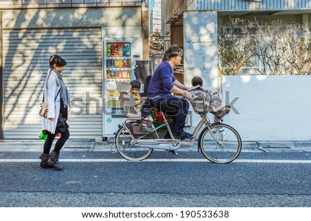 TOKYO, JAPAN - NOVEMBER 23: Japanese Family in Tokyo, Japan on November 23, 2013. Unidentified japanese father carries his children on a bicycle with baby seats