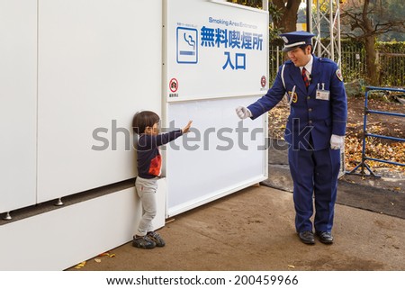 TOKYO, JAPAN - NOVEMBER 26: Smoking area in Tokyo, Japan on November 26, 2013. A security guard plays Rock, Paper, Scissors game with a boy while his parents is in smoking area