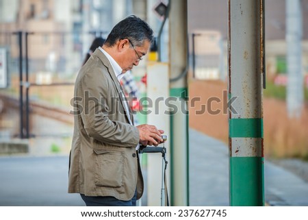KYOTO, JAPAN - OCTOBER 21:  People on a platform in Kyoto, Japan on October 21, 2014. Unidentified Japanese male uses his device while waits for a train on a plateform