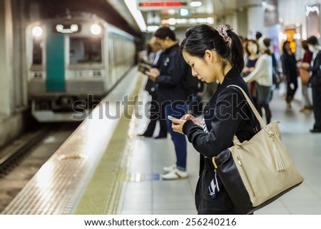 KYOTO, JAPAN - OCTOBER 23: People on a platform in Kyoto, Japan on October 23, 2014. Unidentified Japanese female uses her device while waits for a train on a plateform