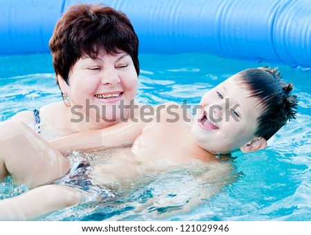 grandmother with a grandchild bath in a pool in blue clean water