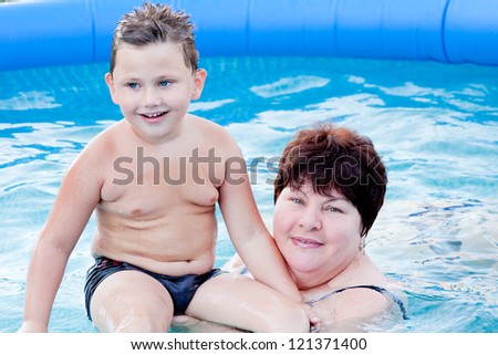 grandmother with a grandchild bath in a pool in blue clean water