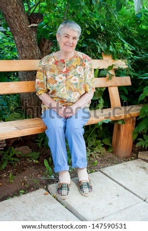 an elderly woman sits on a bench in a garden