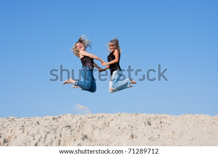 two a young beautiful woman  jumps on a sand-pit  on a background blue sky