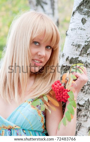 young beautiful woman in a park near a birch with a wild ash in hands