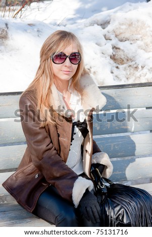 a young woman in a winter park sits on a bench