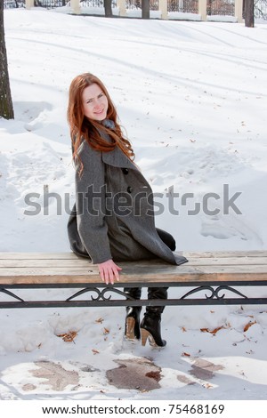 young beautiful woman on a bench in winter in a park