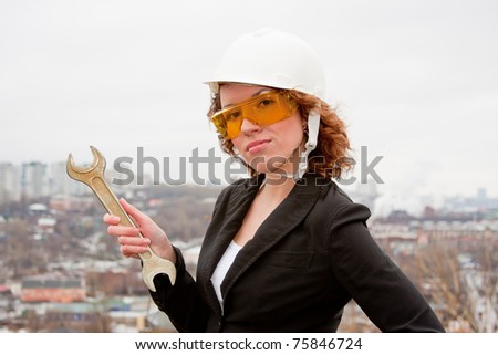 young business woman in a helmet and goggles with a wrench in their hands