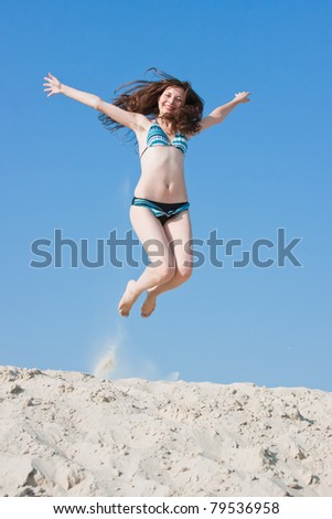 a young beautiful woman in a swimming suit jumps on sand