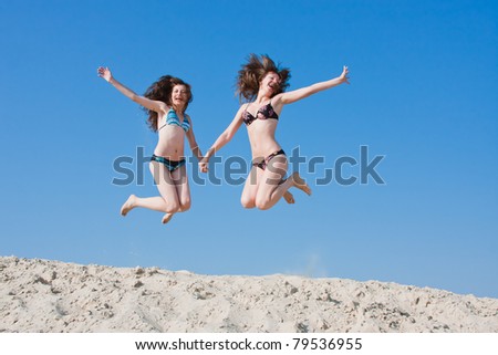two young beautiful women in swimming suits jump on sand