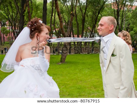 fiancee holds teeth a tie for a groom in a park on nature