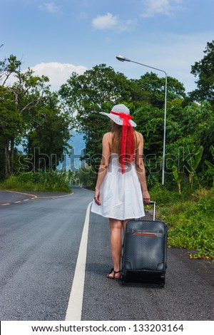 Girl with a suitcase on a deserted road in wild jungle
