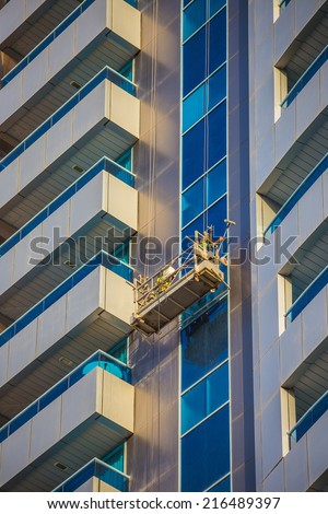 window cleaners in a gondola cleaning the windows of a corporate office skyscraper.